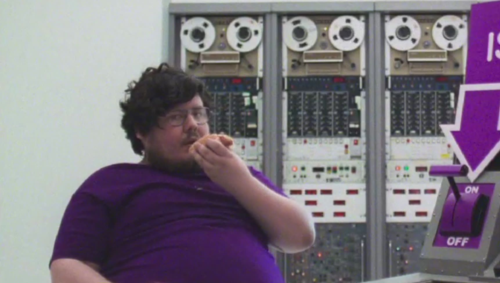 Darren in the E4 control room eating, next to an on/off switch