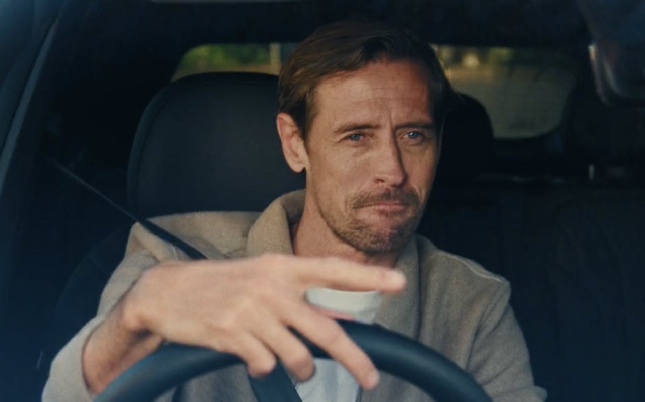 A man in a grey jacket at the wheel of the Chery Tiggo 9, mid-gesture